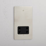 Polished nickel shaver socket with black insert on grey wall. 